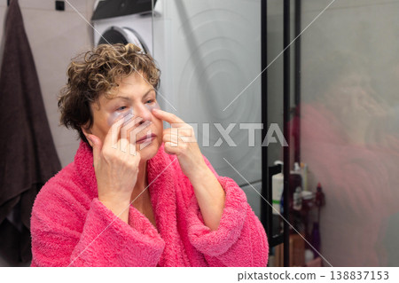 Applying under eye patches mature woman skincare routine in bathroom 138837153