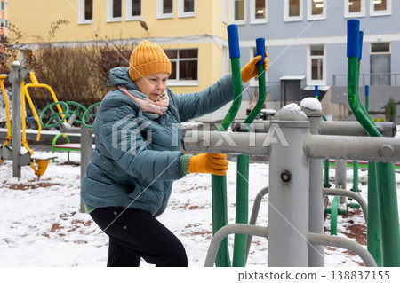 Senior woman exercising on outdoor fitness machine in winter Senior woman exercising on outdoor fitness machine in winter 138837155