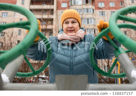 Senior woman exercising on outdoor fitness machine in winter Senior woman exercising on outdoor fitness machine in winter 138837157