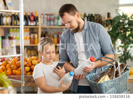 European man with son customer at shop scans QR code on milk bottle using phone camera 138839116