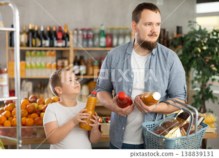 Man with son hold packages plastic bottle and choose consider fruit juice in store Man with son hold packages plastic bottle and choose consider fruit juice in store 138839131