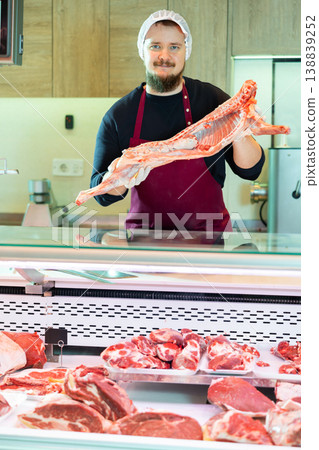 Bearded butcher demonstrating half of fresh lamb carcass at counter Bearded butcher demonstrating half of fresh lamb carcass at counter 138839252