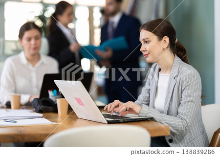 Focused young woman working on laptop during busy corporate session Focused young woman working on laptop during busy corporate session 138839286