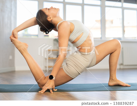 Young attractive smiling woman wearing sportswear practicing yoga, sitting in One Legged King Pigeon exercise in modern yoga studio 138839287