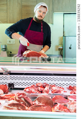 Butcher cuts piece of raw meat for sale in the meat department of supermarket Butcher cuts piece of raw meat for sale in the meat department of supermarket 138839292