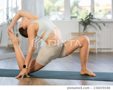 Young attractive smiling woman wearing sportswear practicing yoga, sitting in One Legged King Pigeon exercise in modern yoga studio 138839386