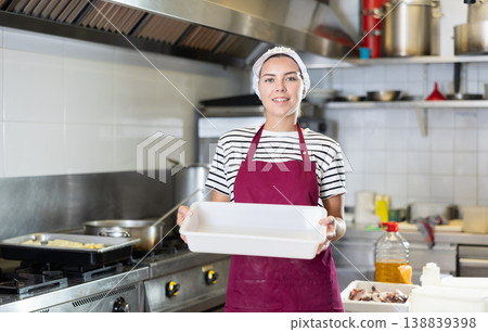 Smiling female worker with empty tray in professional kitchen setting Smiling female worker with empty tray in professional kitchen setting 138839398