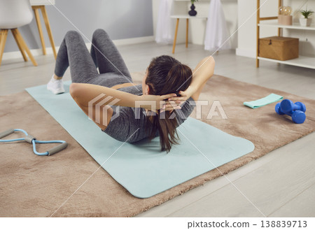 Sporty athletic young woman exercising at home shaking press on floor. 138839713