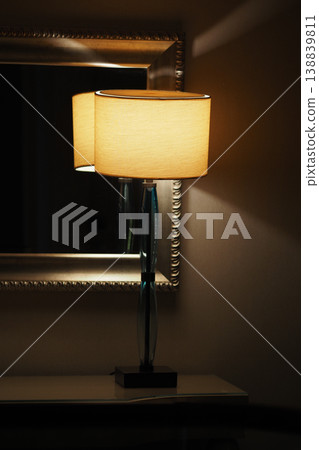 Lamp shines beside mirror in a dimly lit room Lamp shines beside mirror in a dimly lit room 138839811