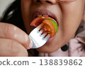 Child uses fork to eat slice of tomato during meal time 138839862
