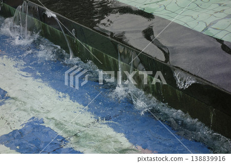 The water overflowing from the fountain park's pool flows down. 138839916