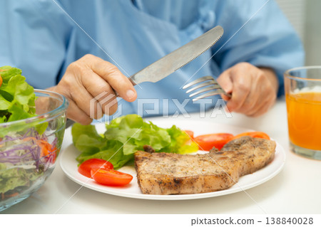 Asian elderly woman patient eating salmon stake and vegetable salad for healthy food in hospital. Asian elderly woman patient eating salmon stake and vegetable salad for healthy food in hospital. 138840028
