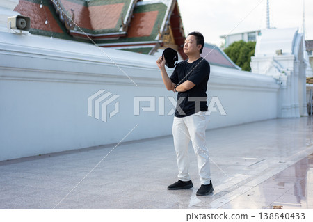 A traveler pauses beside a cultural landmark, taking in the moment with a relaxed and curious attitude. His casual posture reflects the joy of exploring new places on a warm day. 138840433