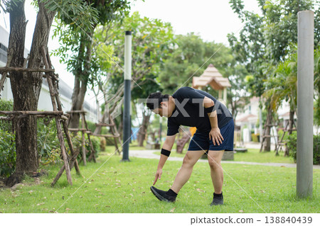 Man wearing sportswear stretches his legs on the grass in a park during an outdoor workout routine. Man wearing sportswear stretches his legs on the grass in a park during an outdoor workout routine. 138840439