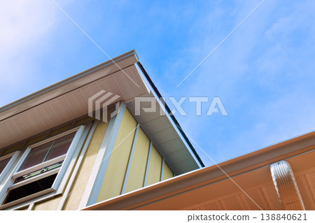 Bright blue sky above house with yellow siding slanted roof edges gutters Bright blue sky above house with yellow siding slanted roof edges gutters 138840621