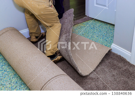 Worker rolls out new carpet in residential hallway during renovation Worker rolls out new carpet in residential hallway during renovation 138840636