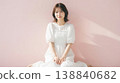 一張日本女性全身照，她坐在粉紅色背景前，沐浴在光線中。 138840682