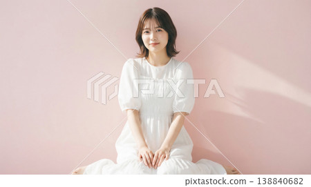 一張日本女性全身照，她坐在粉紅色背景前，沐浴在光線中。 138840682