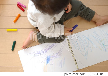 A child drawing pictures with crayons in a sketchbook on the wooden floor of their house. A child drawing pictures with crayons in a sketchbook on the wooden floor of their house. 138841046