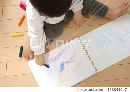 一個孩子在家裡的木地板上用蠟筆在素描本上畫線。 一個孩子在家裡的木地板上用蠟筆在素描本上畫線。 138841047