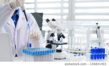Asian adult scientist conducts laboratory experiment pipetting blue liquid into test tube for medical research drug development analysis science innovation 138841401