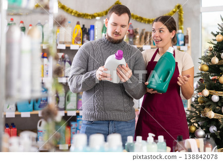 Experienced young female seller offers household liquid detergents to man in store. Christmas shopping Experienced young female seller offers household liquid detergents to man in store. Christmas shopping 138842078