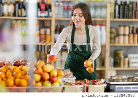 Young saleswoman putting apples on display in grocery Young saleswoman putting apples on display in grocery 138842088