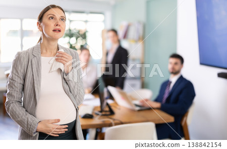 Distressed pregnant woman standing with sad expression in office Distressed pregnant woman standing with sad expression in office 138842154