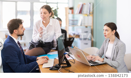 Flirtatious female employee sitting on table and talking to male colleague 138842173