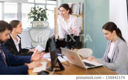 Young woman standing and scolding sad seated colleagues in office Young woman standing and scolding sad seated colleagues in office 138842174