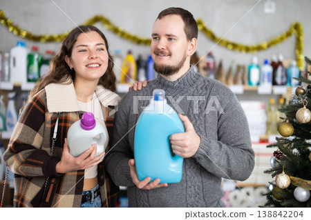 Happy man and woman looking for household liquid detergents on shelves in store. Christmas shopping Happy man and woman looking for household liquid detergents on shelves in store. Christmas shopping 138842204