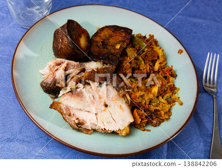Roast pork served with baked potatoes and stewed cabbage 138842206