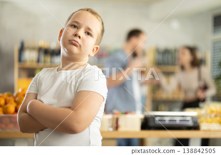 Portrait of capricious offended boy against the backdrop of arguing parents - family quarrel in grocery store Portrait of capricious offended boy against the backdrop of arguing parents - family quarrel in grocery store 138842505