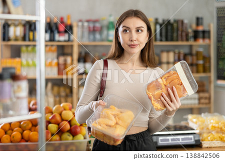 Female buyer carefully reads labels on packaging of semi-finished chicken products - she chooses best product in supermarket Female buyer carefully reads labels on packaging of semi-finished chicken products - she chooses best product in supermarket 138842506