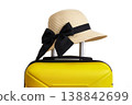 Stylish straw hat with black ribbon on a yellow suitcase against a white background.  138842699