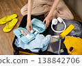 A woman puts hygiene products, clothes, a travel guide, headphones and travel accessories in a suitcase 138842706