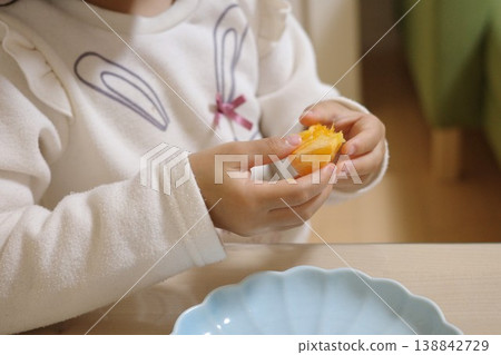 A child's hands eating a mandarin orange from a light blue plate at home. A child's hands eating a mandarin orange from a light blue plate at home. 138842729