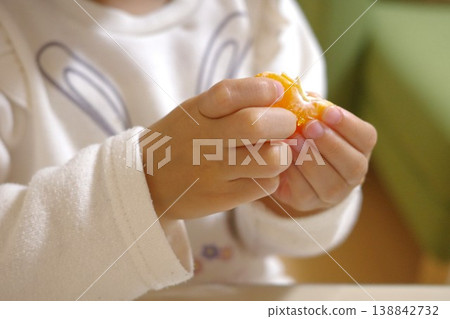 A child's hands diligently peeling an orange at home. A child's hands diligently peeling an orange at home. 138842732