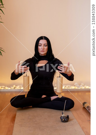Sound therapy. Relaxing process. Woman doing ritual with traditional wind chime instrument on meditation session in balance pose in studio. Sound therapy. Relaxing process. Woman doing ritual with traditional wind chime instrument on meditation session in balance pose in studio. 138843309