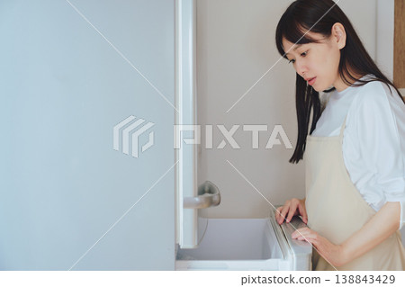 一位女士打開冰箱,檢視裡面的東西。日常生活和備餐場景。 一位女士打開冰箱,檢視裡面的東西。日常生活和備餐場景。 138843429