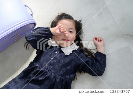 A sleepy-looking Japanese girl with a schoolbag lying on the floor. 138843707