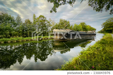 A Serene Reflection on a Tranquil Canal Featuring an Abandoned Barge Awaiting Exploration A Serene Reflection on a Tranquil Canal Featuring an Abandoned Barge Awaiting Exploration 138843976
