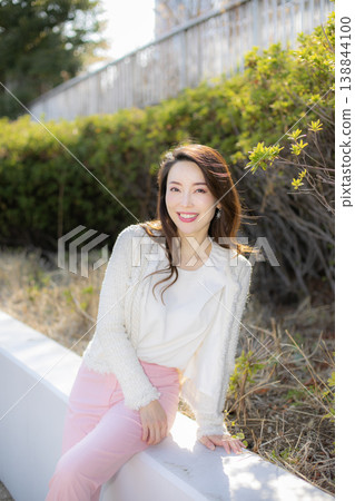 一位年輕女子在公園的灌木叢旁休息。 一位年輕女子在公園的灌木叢旁休息。 138844100