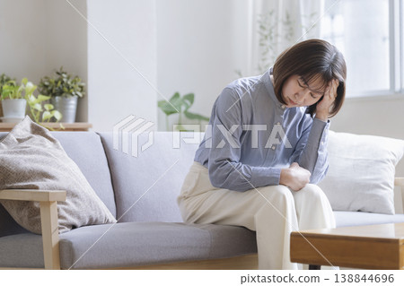一位四十多歲的婦女坐在沙發上,雙手抱頭。 一位四十多歲的婦女坐在沙發上,雙手抱頭。 138844696