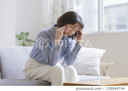 一位四十多歲的婦女坐在沙發上，雙手抱頭。 138844744