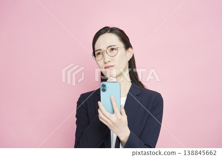 A businesswoman struggling with her smartphone (pink background) A businesswoman struggling with her smartphone (pink background) 138845662