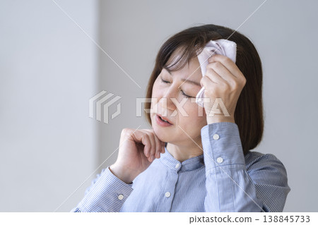 A woman in her late 40s wipes the sweat from her forehead. A woman in her late 40s wipes the sweat from her forehead. 138845733