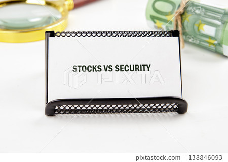 White card displaying Stocks vs Security in a black holder, with a rolled 100 Euro banknote and a magnifying glass on a white surface White card displaying Stocks vs Security in a black holder, with a rolled 100 Euro banknote and a magnifying glass on a white surface 138846093