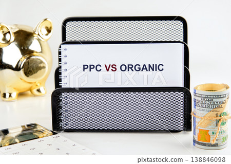 A desk setup presents a notebook with PPC versus organic marketing, financial items like a golden piggy bank, cash, and a calculator A desk setup presents a notebook with PPC versus organic marketing, financial items like a golden piggy bank, cash, and a calculator 138846098