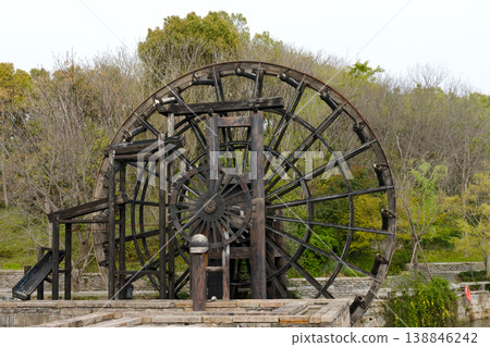 Historic Wooden Waterwheel Mill Surrounded by Green Trees and Stone Terrace in Park Setting 138846242